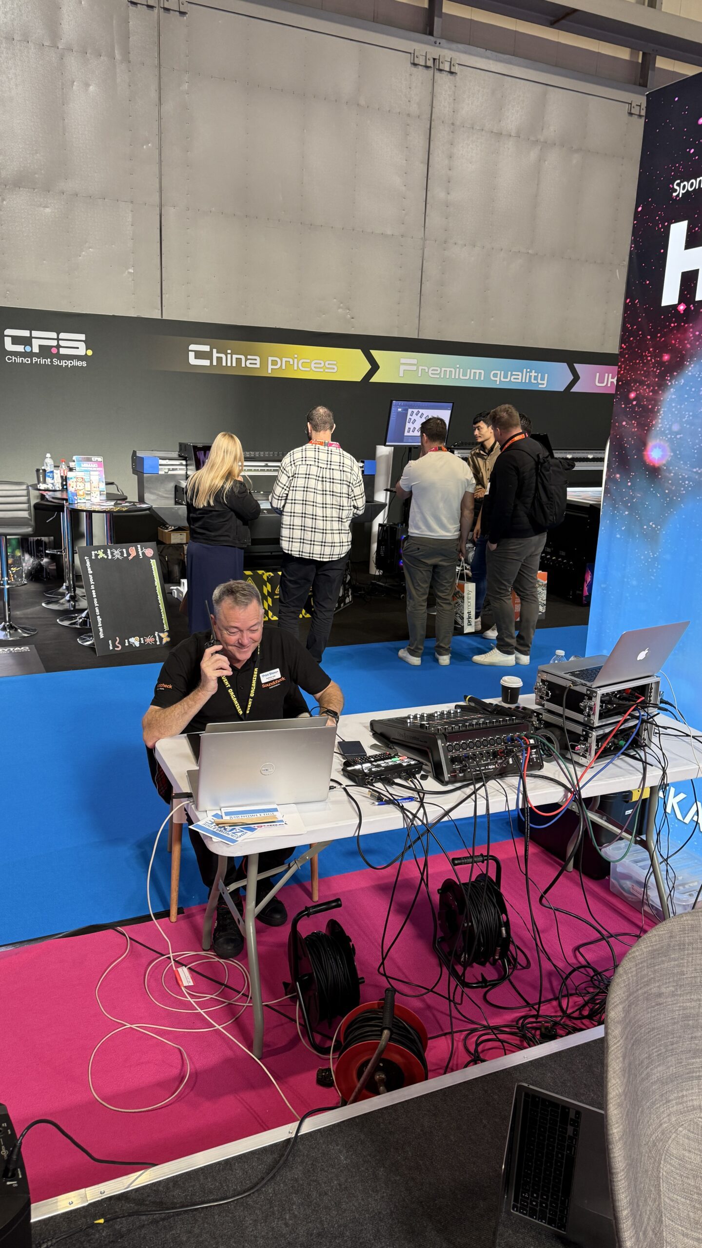 Andrew Lake working at a fold-out table backstage at The Print Show, coordinating on the phone