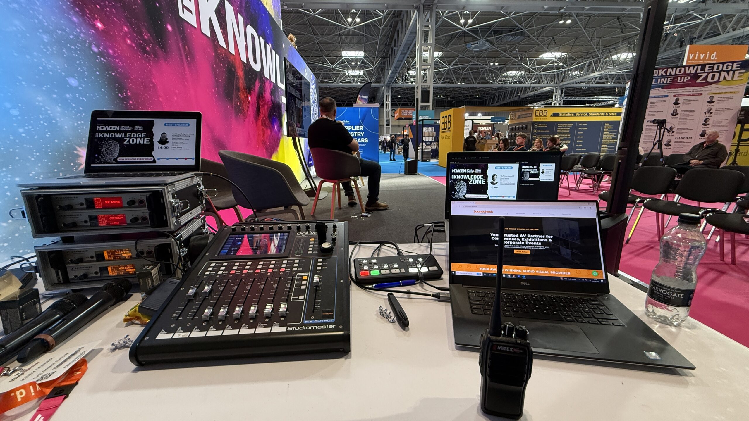 The AV control desk for the Knowledge Zone, with mixer, wireless microphones and laptops running the schedule