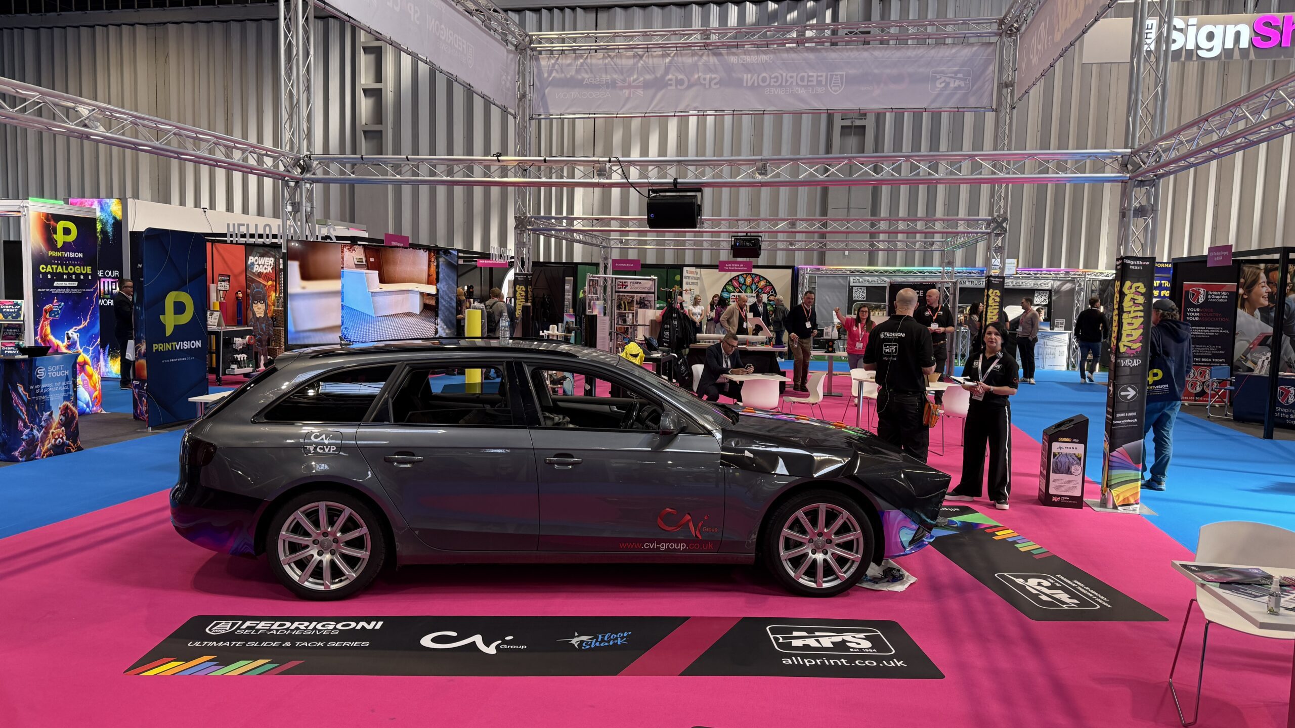 School of Wrap at The Print Show 2025, showing the partially wrapped car, rigged truss and screens on the show floor